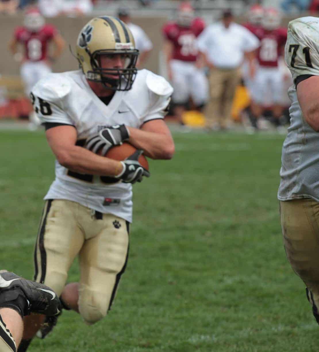 Youth football player in uniform running with the ball on the field.